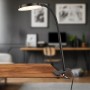 Schwarze Briloner LED-Klemmleuchte PLEGG mit Lichtkante am Tisch befestigt.