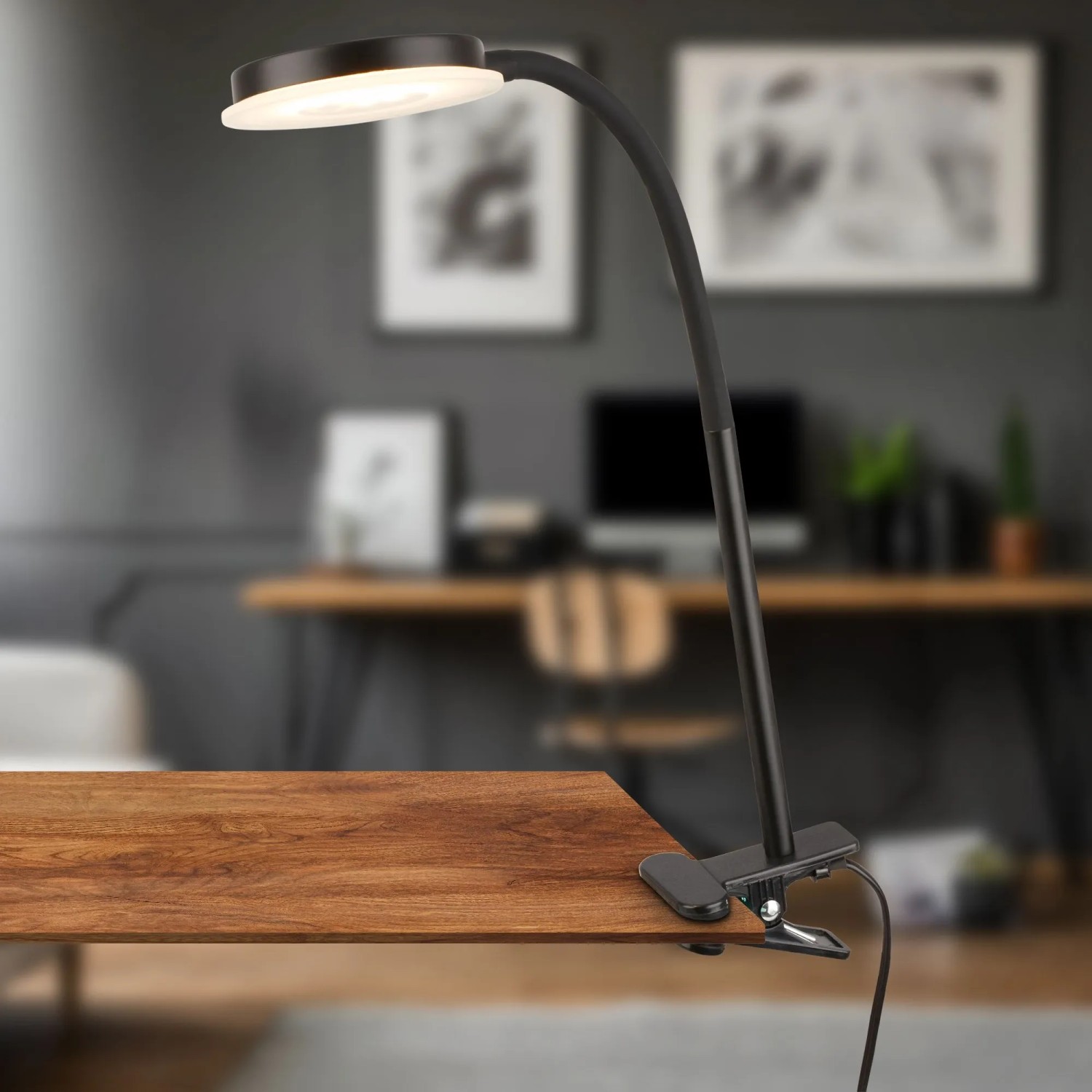 Schwarze Briloner LED-Klemmleuchte PLEGG mit Lichtkante am Tisch befestigt.
