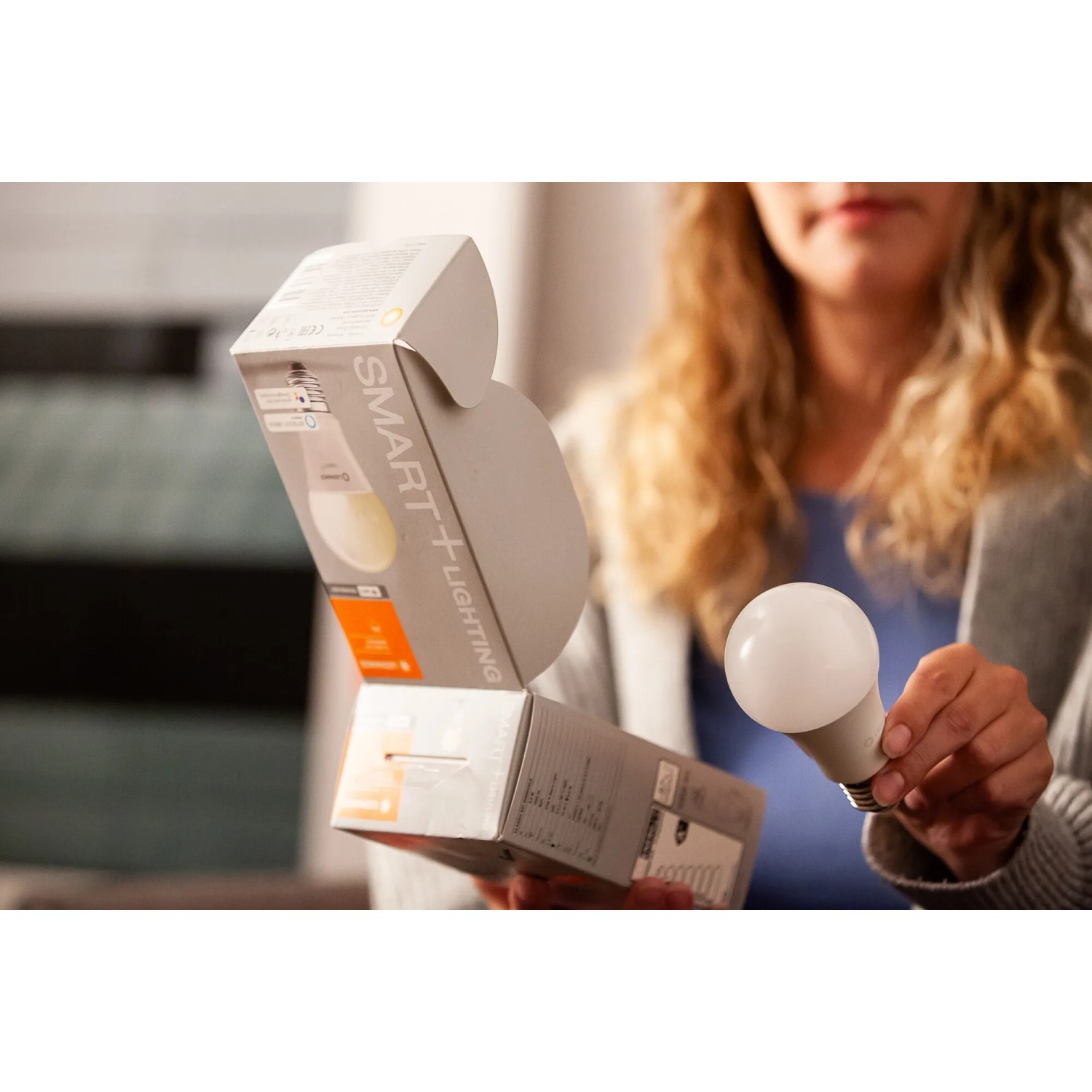 Ledvance Smart+ Leuchtmittel E27 in Weiß, mit Verpackung und Hand, die das Leuchtmittel hält.