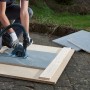 Wolfcraft Absaughaube mit Führungsschlitten für Winkelschleifer im Einsatz beim Fliesenschneiden.