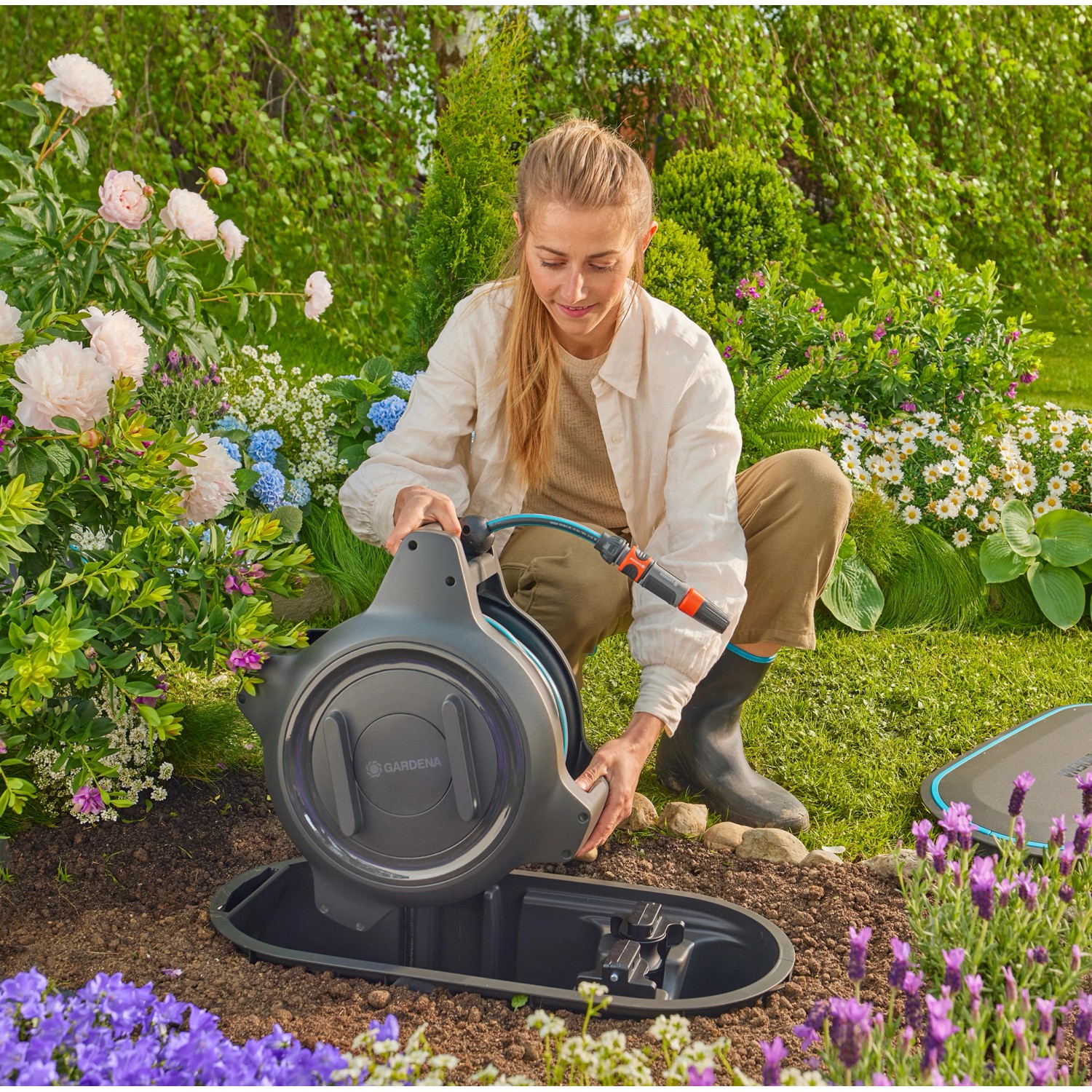 Frau installiert Gardena Undercover Schlauchbox RollUp M im Garten.