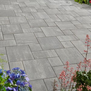 Verlegte, graue Mehrformat-Pflastersteine Talessio Beton Grau-Alpin mit Blumen.