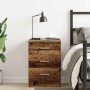 Nachttisch in Altholz-Optik mit 3 Schubladen und Metallgriffen im Schlafzimmer neben Bett und Lampe.