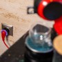Shelly Smart-Stecker Plug S Gen3 Schwarz in Steckdose mit Kaffeemaschine im Hintergrund.