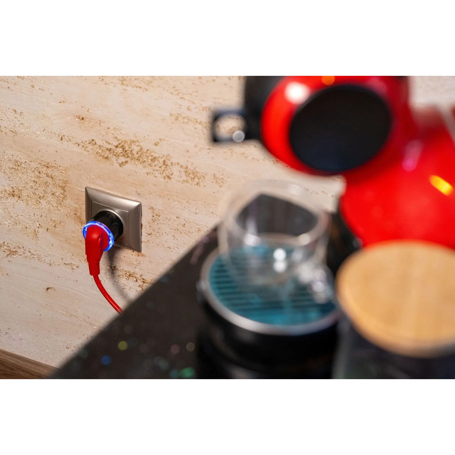Shelly Smart-Stecker Plug S Gen3 Schwarz in Steckdose mit Kaffeemaschine im Hintergrund.