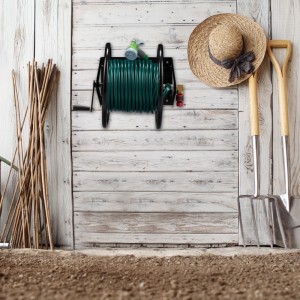 Schwarzer Relaxdays Wand-Schlauchaufroller aus Stahl mit grünem Gartenschlauch an heller Holzwand, umgeben von Gartenwerkzeugen.