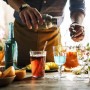 Person gießt aus Edelstahl Shaker in Glas. 5-teiliges Cocktailset für Mixgetränke auf Holztisch, Party.