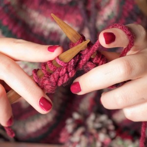 Hände stricken mit natürlichen Bambus-Stricknadeln und pinker Wolle. Nahaufnahme des Nadelspiels in Aktion.