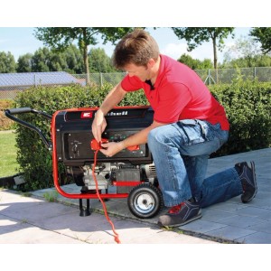 Mann schließt rotes Kabel an mobilen Einhell Stromerzeuger TC-PG 55 E5 an. Benzin Generator mit Rädern im Garten.
