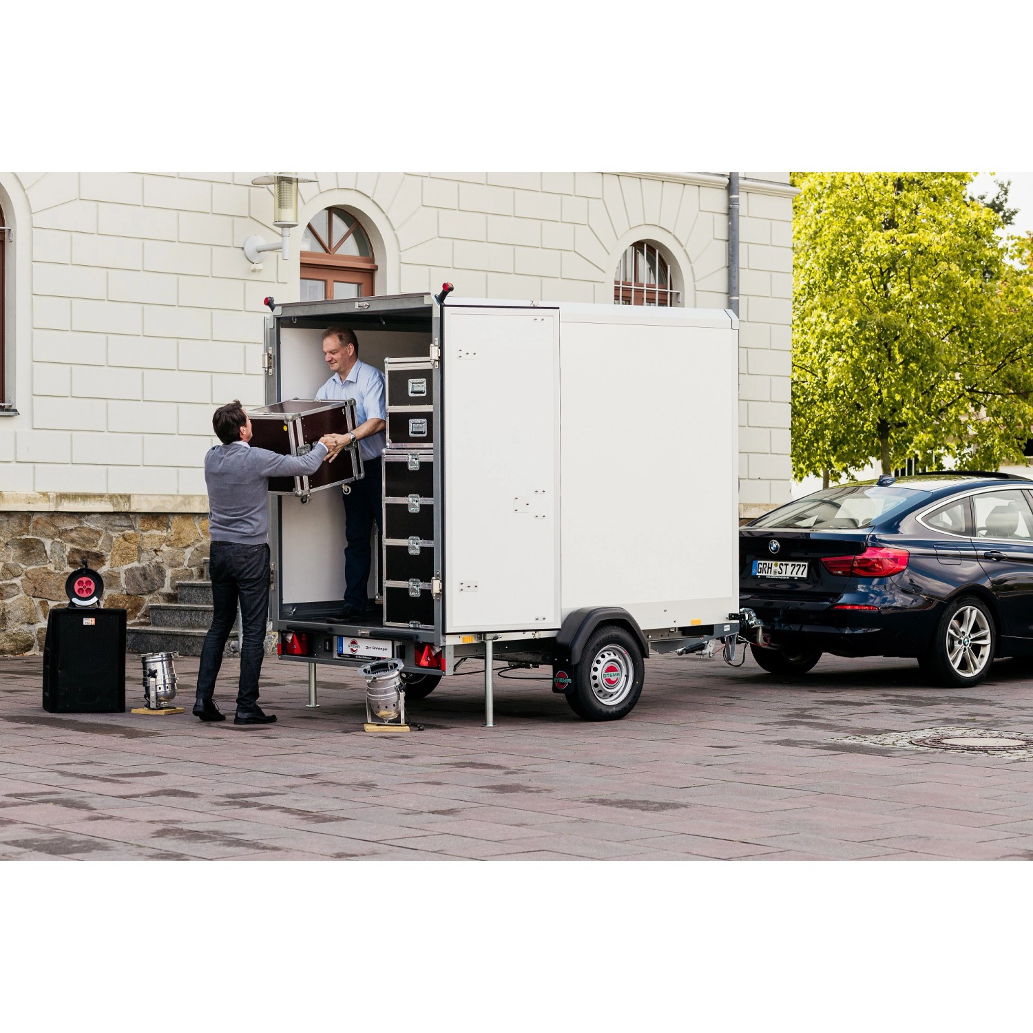 Stema Kofferanhänger 1300 Sandwich beladen mit Koffern, gezogen von einem PKW.