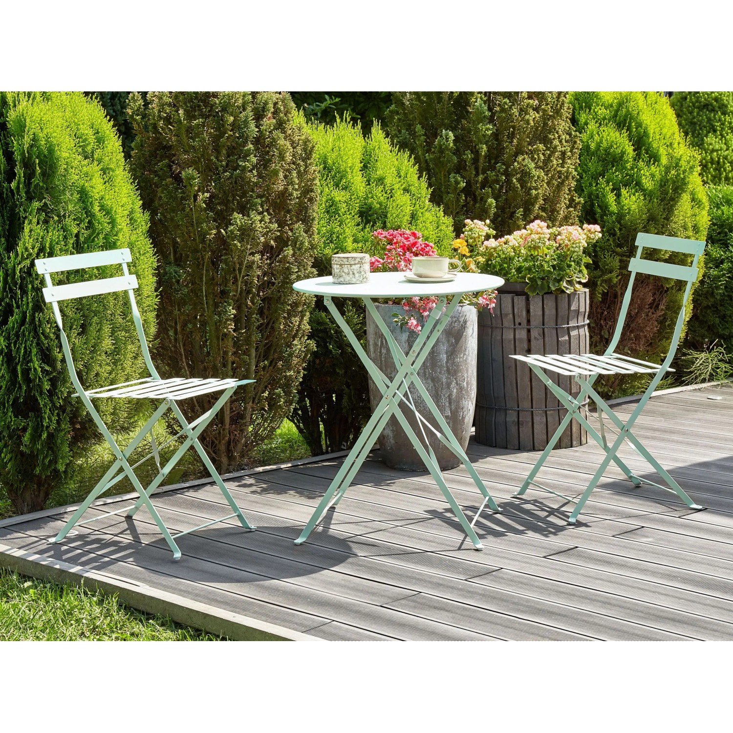 Mintgrünes Beliani Bistro Set FIORI: runder Metalltisch, zwei klappbare Gartenstühle auf Holzterrasse.