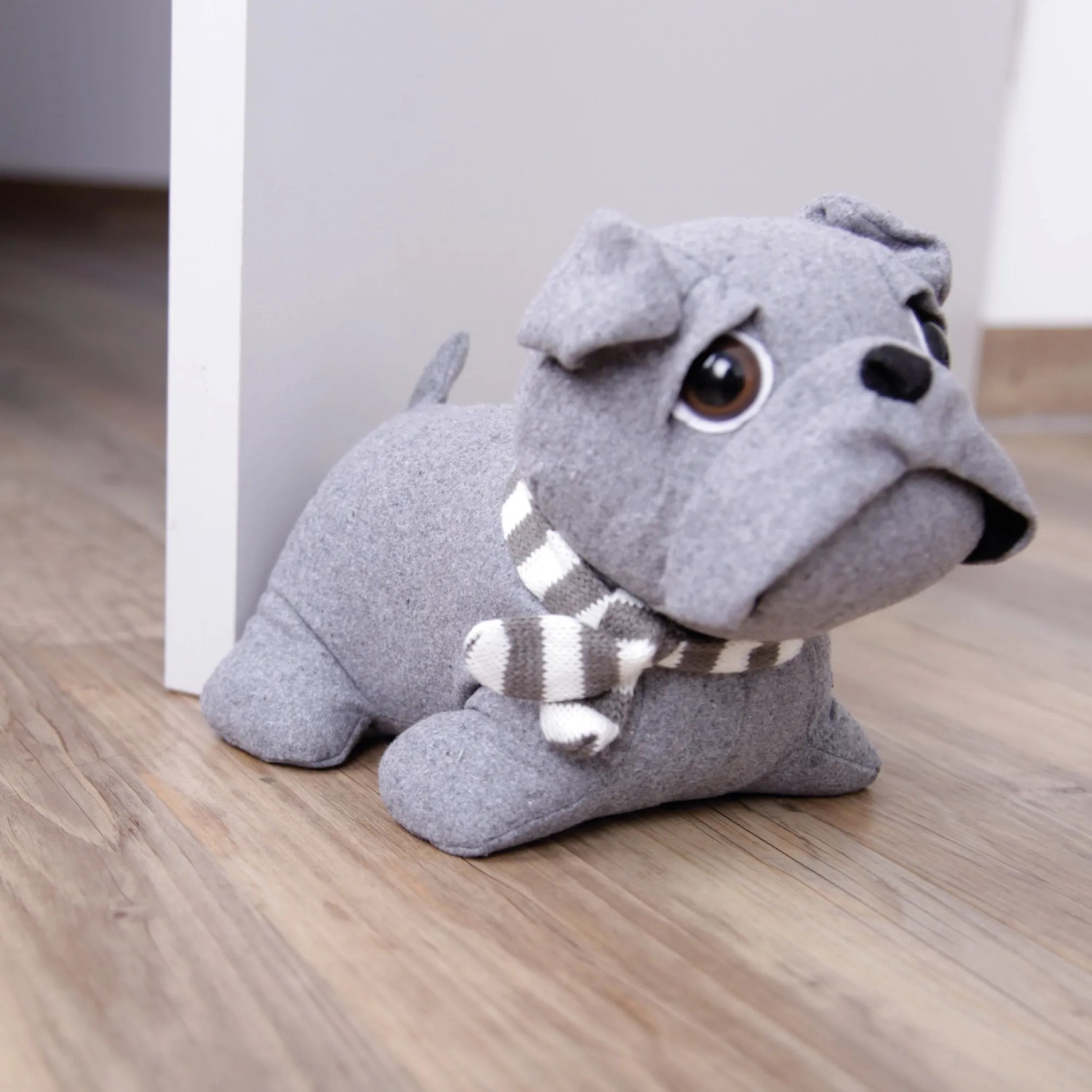 Grauer Bestlivings Türstopper Mops/Bulldogge (25x20cm) mit Schal vor weißer Tür auf Holzboden.