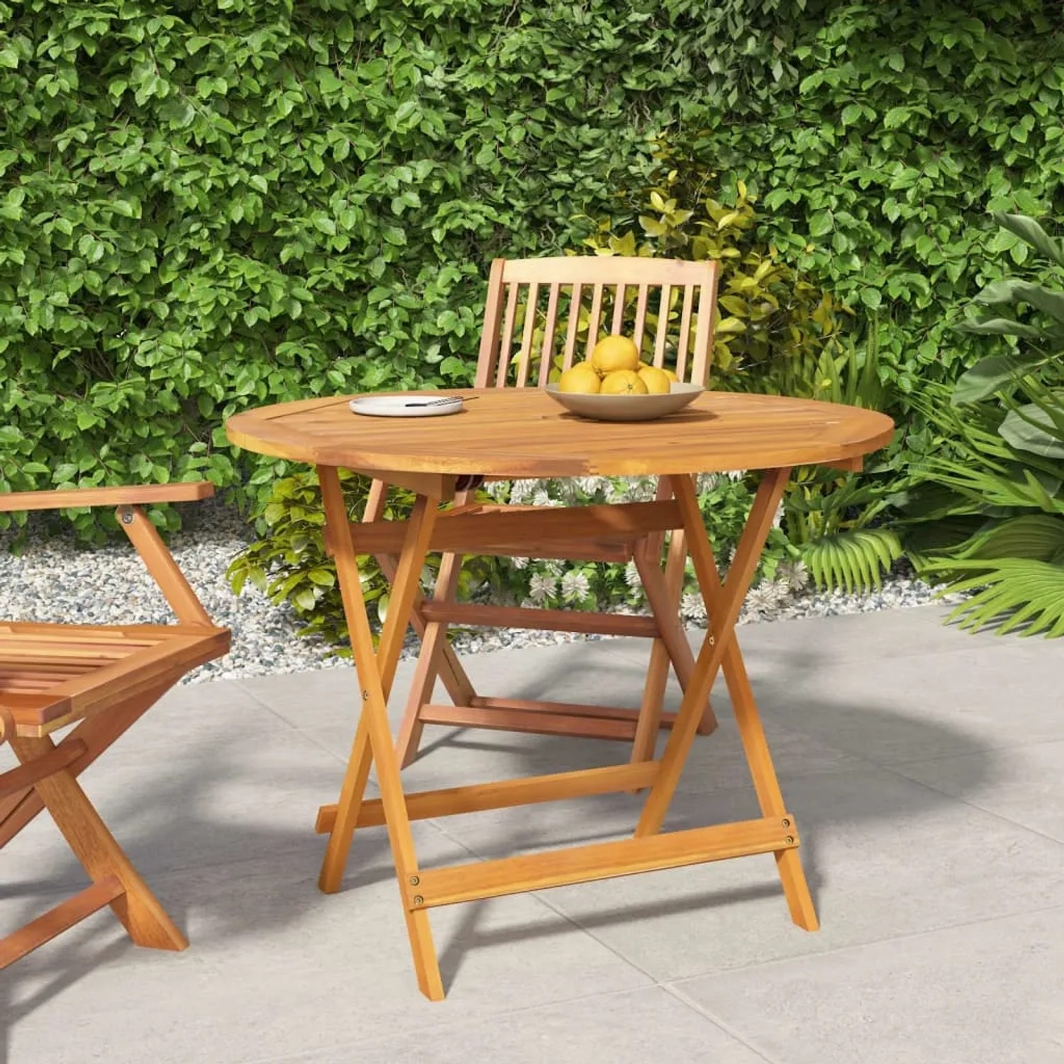 Klappbarer Gartentisch aus Akazienholz, Ø 90 cm, mit Stuhl und Zitrone auf dem Tisch.