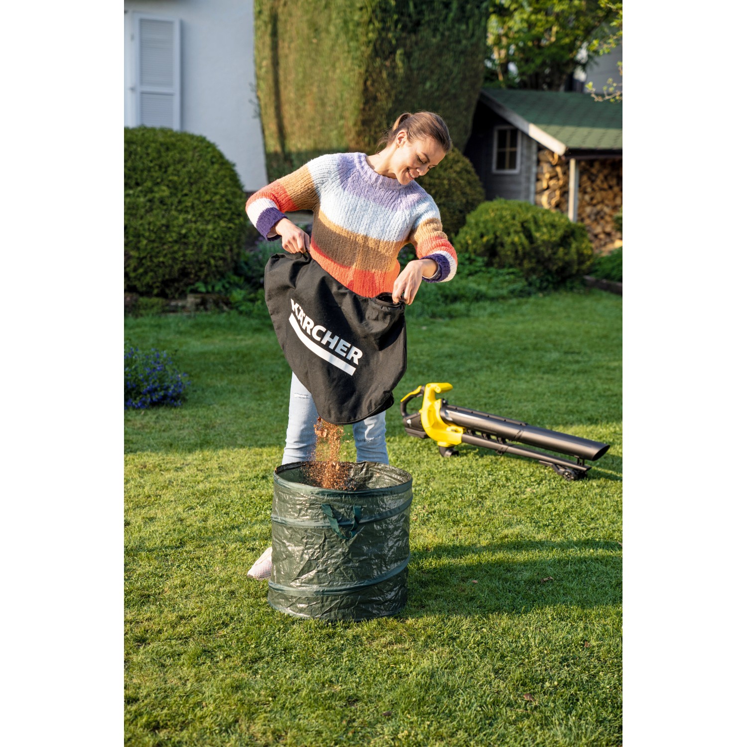 Frau leert Laubsack des Kärcher Akku-Laubsauger BLV 18-200 in Gartensack. Laubbläser im Hintergrund.