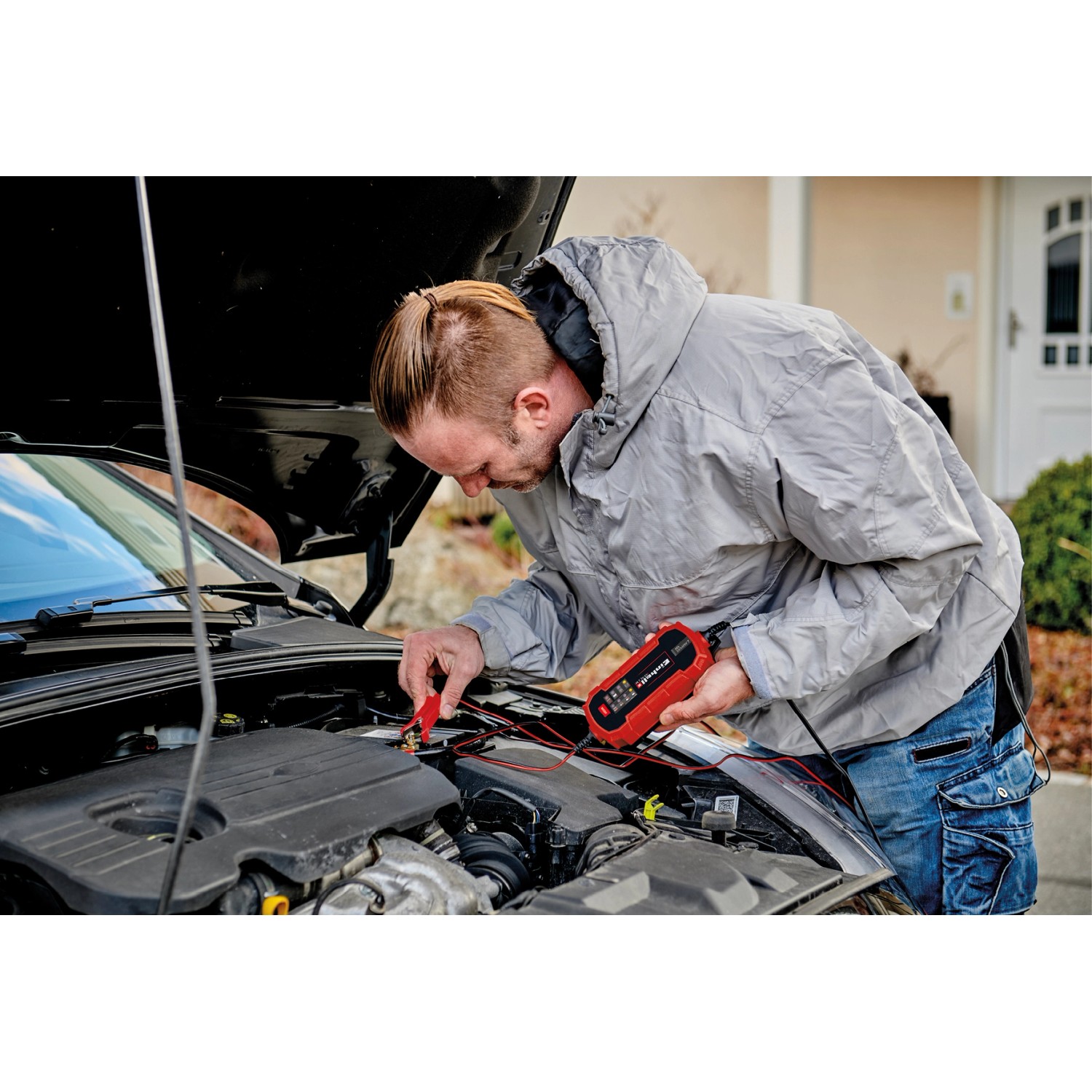 Mann schließt Einhell CE-BC 2 M Batterieladegerät an Autobatterie an.