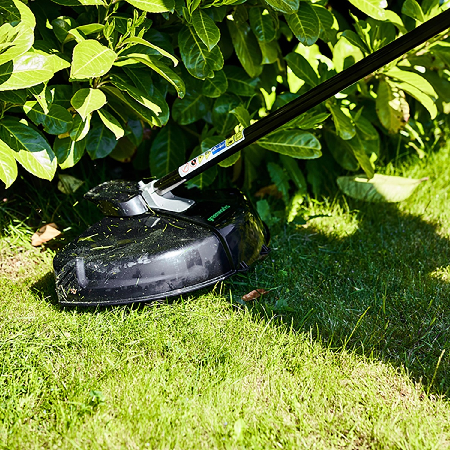 Greenworks Akku-Rasentrimmer GD40BC beim Trimmen von Rasenkanten unter Büschen.