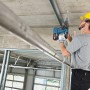 Handwerker bohrt mit blauem Bosch Professional Akku-Bohrhammer GBH 18V-26 in Betondecke. Baustelle, kabelloses Bohren.