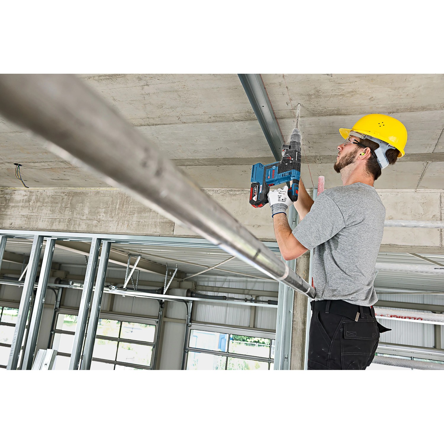 Handwerker bohrt mit blauem Bosch Professional Akku-Bohrhammer GBH 18V-26 in Betondecke. Baustelle, kabelloses Bohren.