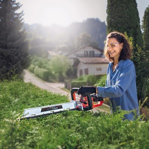 Frau schneidet Hecke mit Einhell Akku-Heckenschere Arcurra 18/55. Kabellose Gartenarbeit.