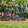 Pinkes Salta Bodentrampolin Comfort Edition (ø 251 cm) mit Sicherheitsnetz und springendem Kind im Garten.