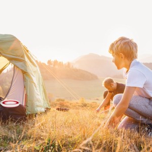Camping-Szene mit Zelt und rotem Relaxdays Falteimer im Gras, zwei Personen im Hintergrund.