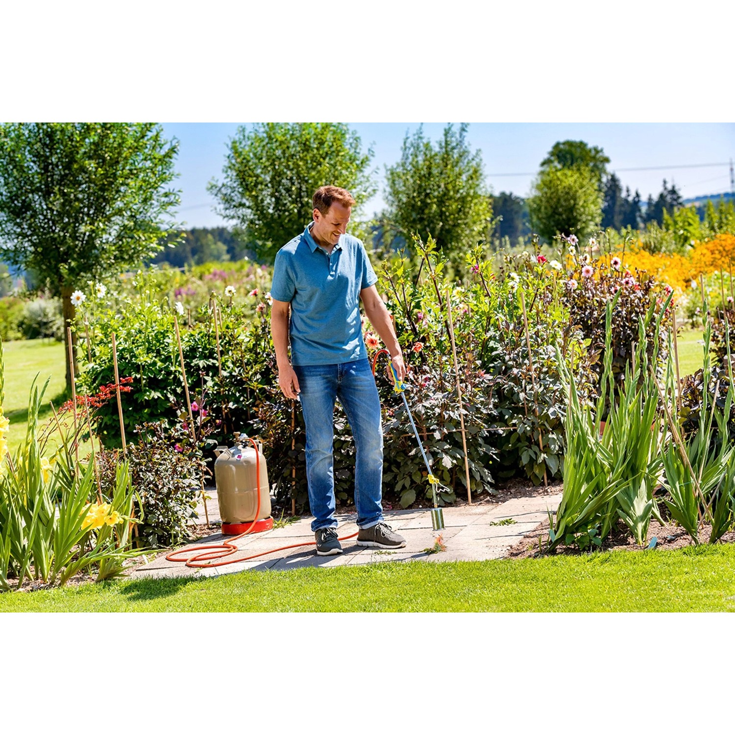 Mann nutzt Gloria Thermoflamm bio Professional Plus Unkrautbrenner im Garten mit Gasflasche.