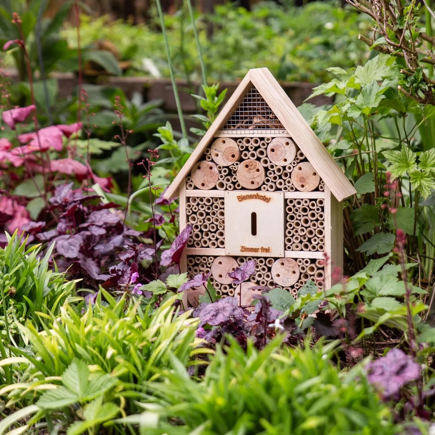 Holz Insektenhotel für Bienen und Nützlinge im Garten. Hausform mit Bambusröhren und Nistkammern.