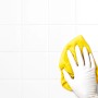 Hand mit weißem, latexfreiem Einmalhandschuh reinigt weiße Fliesen mit gelbem Tuch.