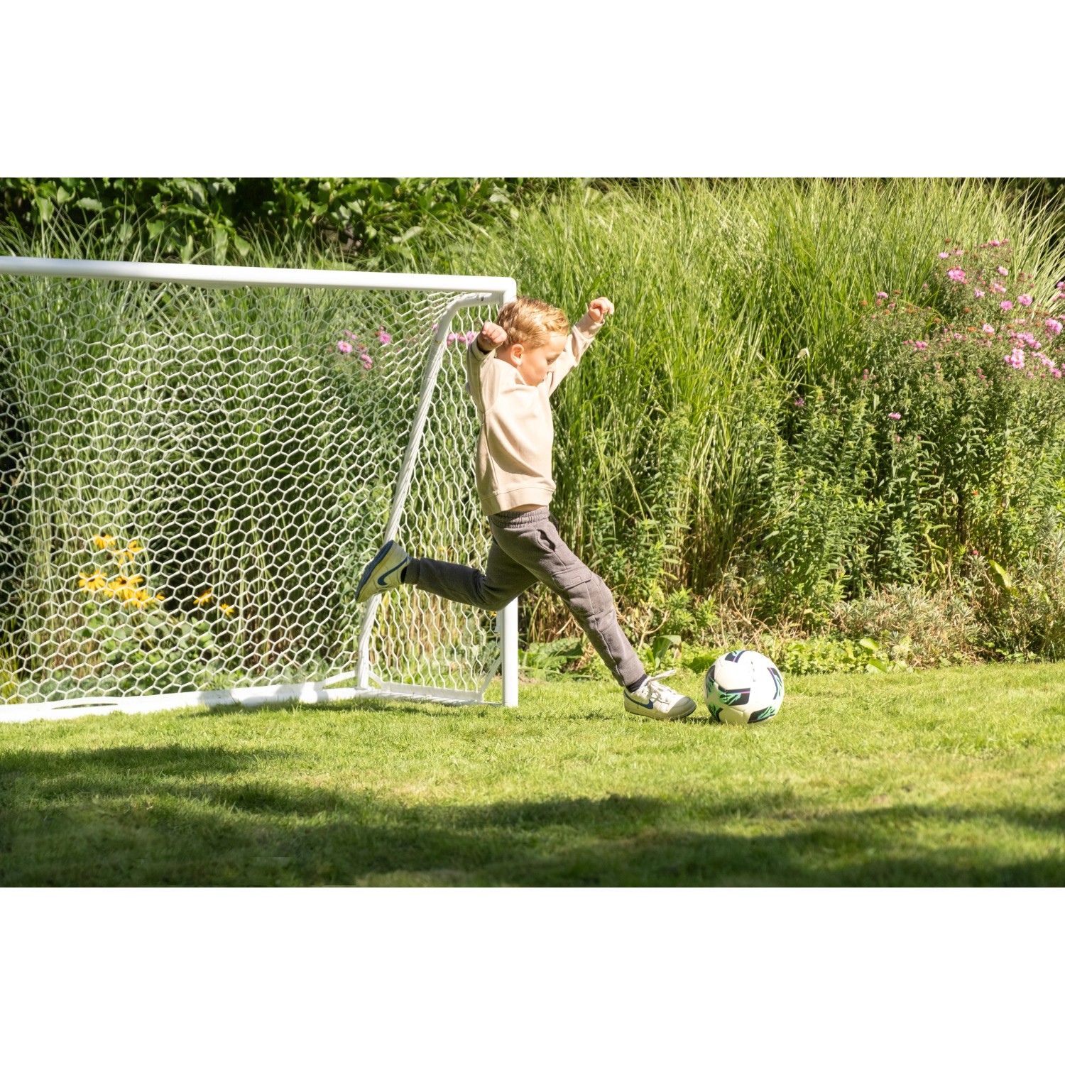 Junge schießt Ball vor Exit Fußballtor Scala Aluminium 180x120 cm Weiß im Garten.