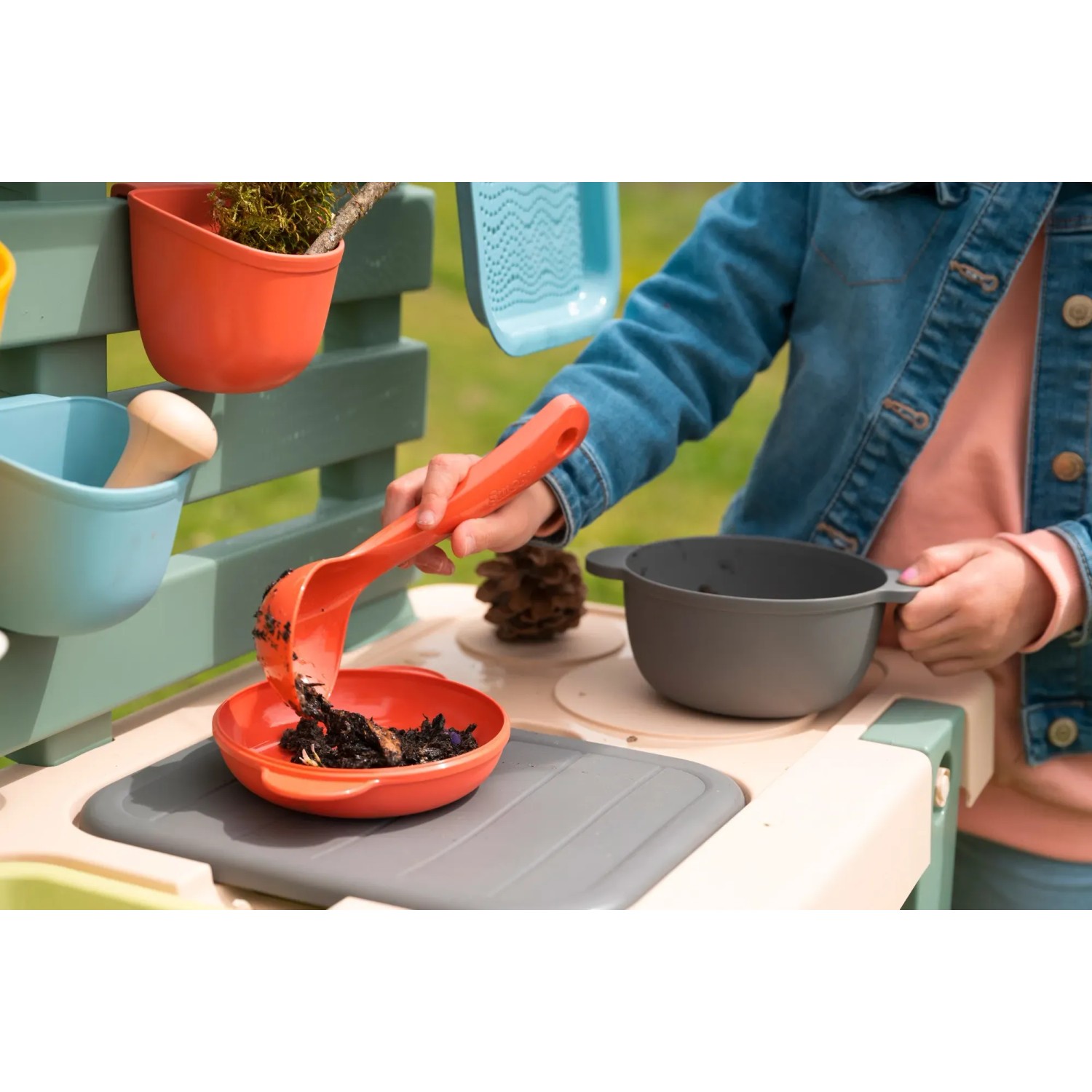 Kind spielt mit Smoby Matschküche Life: Rote Schüssel und Schöpfkelle mit Erde.