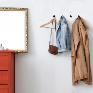 Drei schwarze SOTECH TALEA Garderobenhaken aus Edelstahl an weißer Wand, mit Jacke, Tasche und Mantel. Modernes Design für Flur.