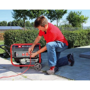 Mann schließt rotes Kabel an Einhell Benzin-Stromerzeuger an. Mobiler Stromgenerator mit Rädern im Garten.