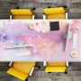 Bunte Tulup Schreibtischunterlage mit rosa, lila Aquarell-Design auf Holztisch, mit PCs und gelben Stühlen. Schützt den Arbeitsplatz.
