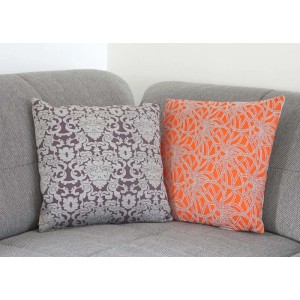 2er Set Deko-Kissen 45x45cm: ein dunkelgraues mit Barockmuster, ein oranges mit Blumenmuster auf Sofa.