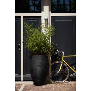 Schwarzer Capi Pflanztopf Nature Rib Elegant Deluxe, Ø 40x60 cm, vor dunkler Haustür mit Fahrrad.