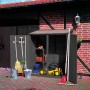 Großer, anthrazitfarbener Promadino Geräteschrank aus Holz mit Gartengeräten und Rasenmäher.