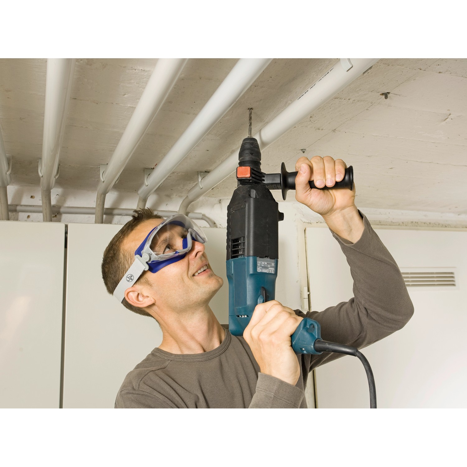 Mann bohrt mit LUX Schutzbrille mit Band Grau ein Loch in die Decke.
