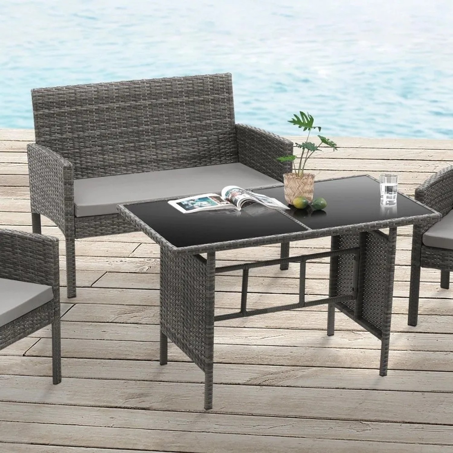 Graue Svita Brooklyn XL Rattan Garten Essgruppe: Tisch mit Glasplatte, 2er Sofa, Sessel und hellgrauen Kissen auf Holzdeck.
