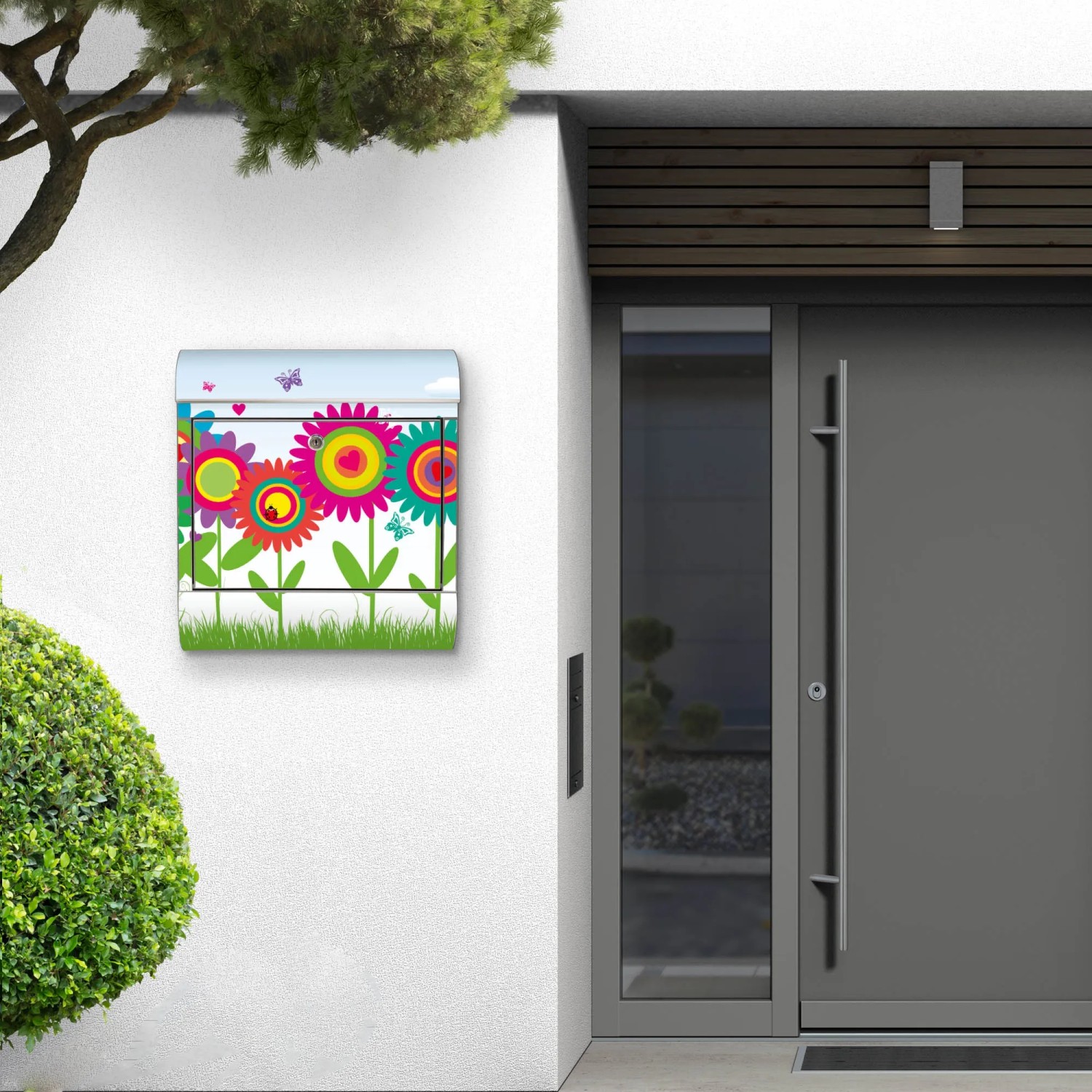 Edelstahl Briefkasten mit buntem Blumenmotiv und Zeitungsfach an einer weißen Hauswand.