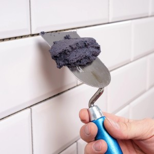 Auftragen von grauer Knauf Flexfuge smart Fugenmasse auf weiße Fliesen mit einer Spachtel.