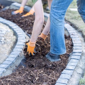 Person verteilt Rindenmulch (0-40 mm) im Gartenbeet mit Steineinfassung.