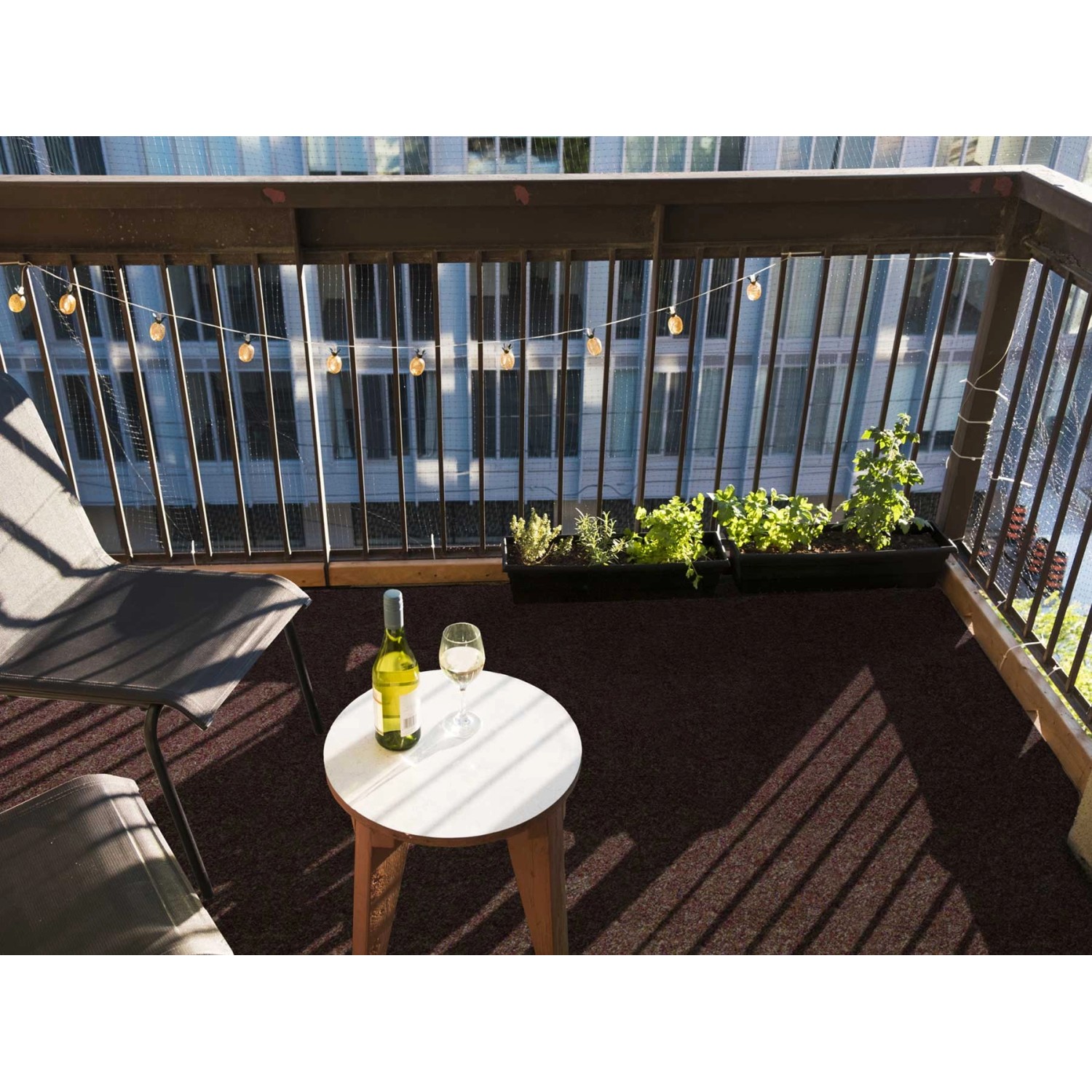 Primaflor Rasenteppich Green Braun auf Balkon mit Tisch, Stuhl, Wein und Lichterkette.