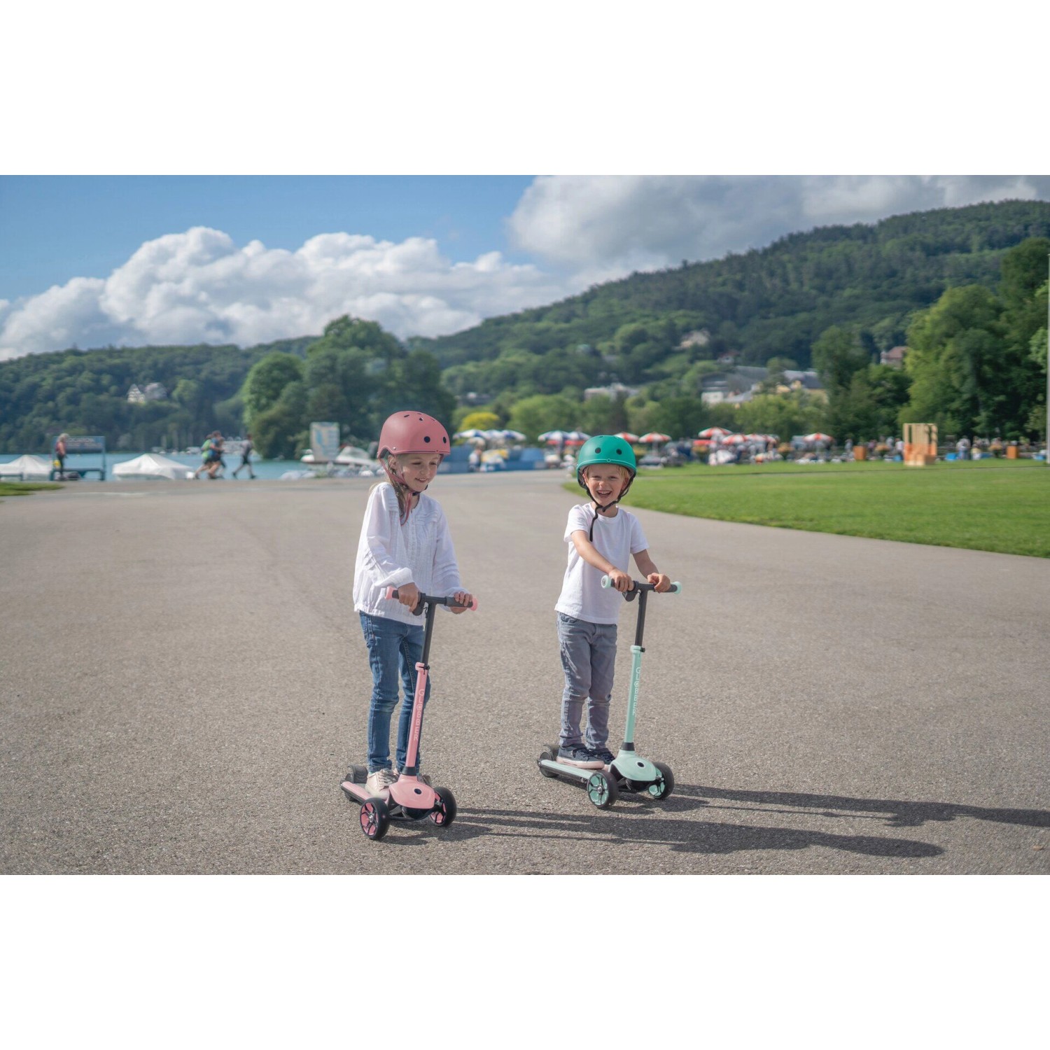 Zwei Kinder mit mintfarbenem und pinkem Globber E-Scooter One K E-Motion 4 Plus auf Asphalt.