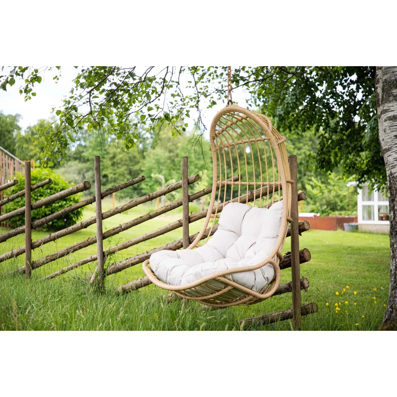 Hängender Pulau Gartenstuhl mit Kissen in Natur vor Gartenkulisse.