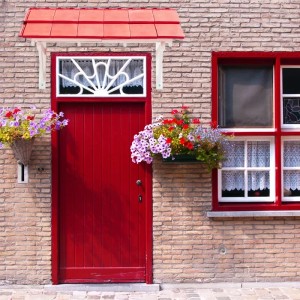 Kordo Vordach 139cm aus Holz über roter Haustür mit Blumenampeln und rotem Ziegeldach.