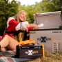 Cross Tools Travelbox 500 Power Station beim Camping mit Kühlbox und Zelt im Hintergrund.