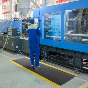 Schwarze KARAT Anti-Ermüdungsmatte mit gelben Rändern im Einsatz vor Industriemaschine.
