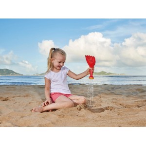 Mädchen spielt am Strand mit roter Hape Regenschaufel aus Kunststoff. Sandspielzeug für Kinder.