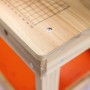 Detailansicht der OBI Kinderwerkbank aus Holz: helle Holzplatte mit aufgedrucktem Raster, abgerundete Kanten, orangefarbene Ablage.