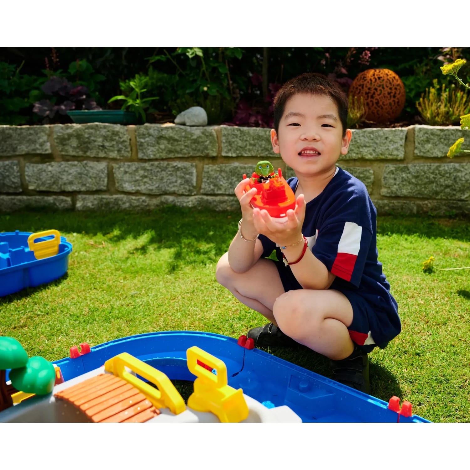 Kind spielt mit AquaPlay MountainLake Wasserbahn. Buntes Spielset mit Boot und Spielfigur im Garten.